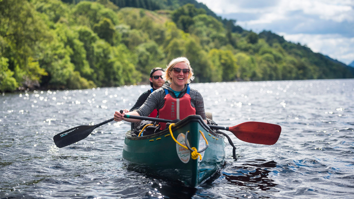 Two people enjoying a canoe trip on a tree-lined lake